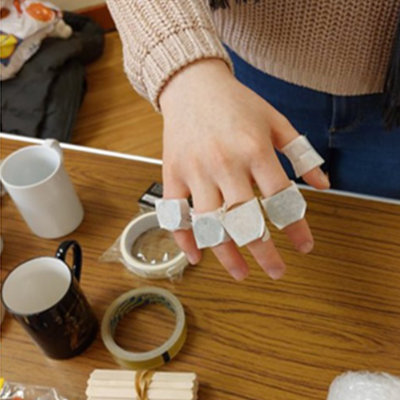A student has coins taped to their knuckles to simulate the experience of having arthritis and how it affects hand control.